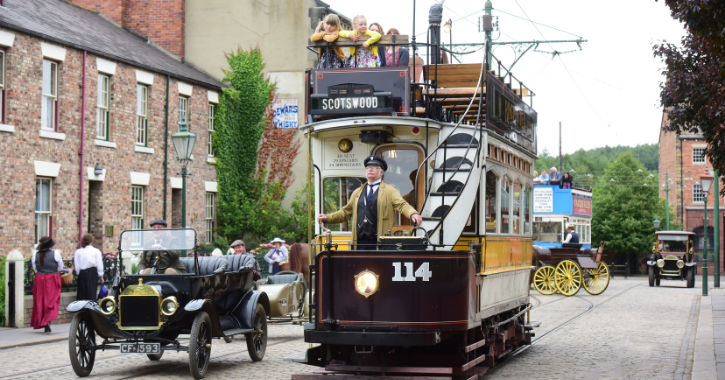 View of the 1900s town at Beamish Museum with people onboard the tram alongside a historic car.